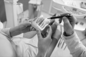 Dental professional in Derby explaining a dental implant using a teeth model, highlighting the implant with a pen